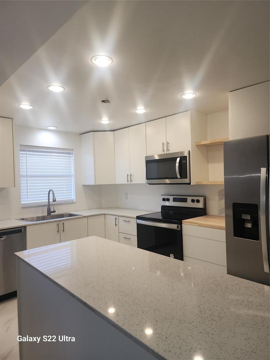 A modern kitchen features white cabinets, stainless steel appliances, and a light-colored quartz island countertop — 700 SE 6th Avenue # 111, Deerfield Beach FL 33441, DEERFIELD BEACH, FL