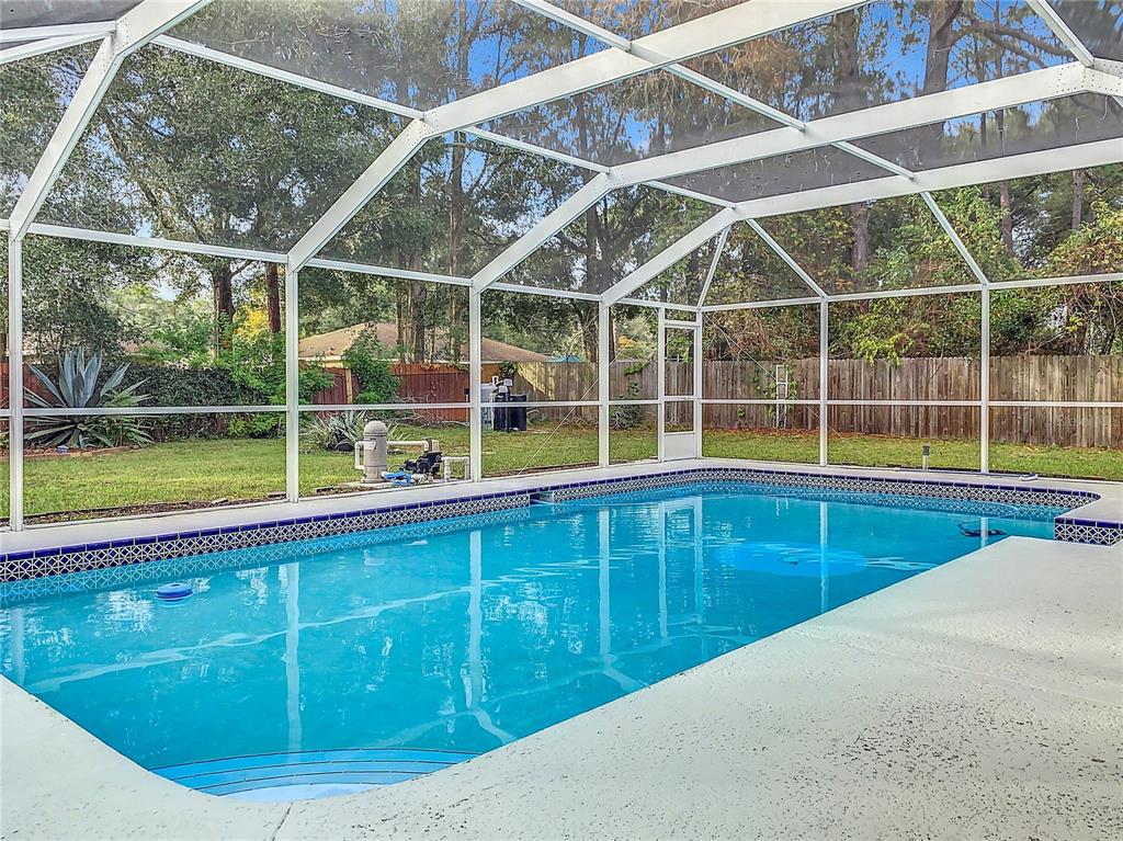A single-story peach-colored house with white shutters sits behind a tall green hedge — 6170 NW 57TH COURT, OCALA, FL