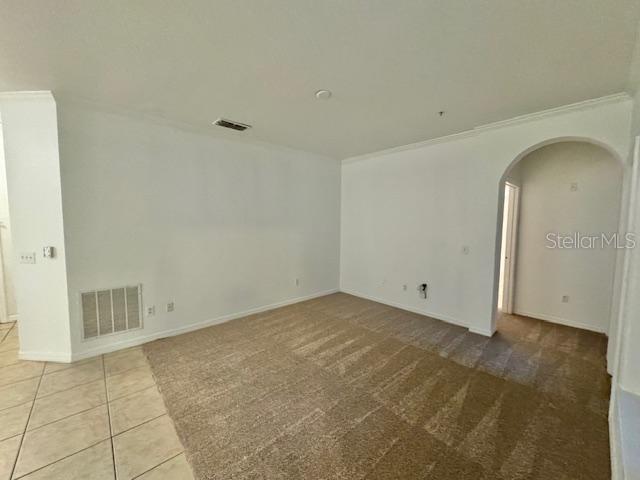An empty room features beige carpeting, tile flooring, white walls, and an arched doorway — 3611 CONROY UNIT 818, ORLANDO, FL