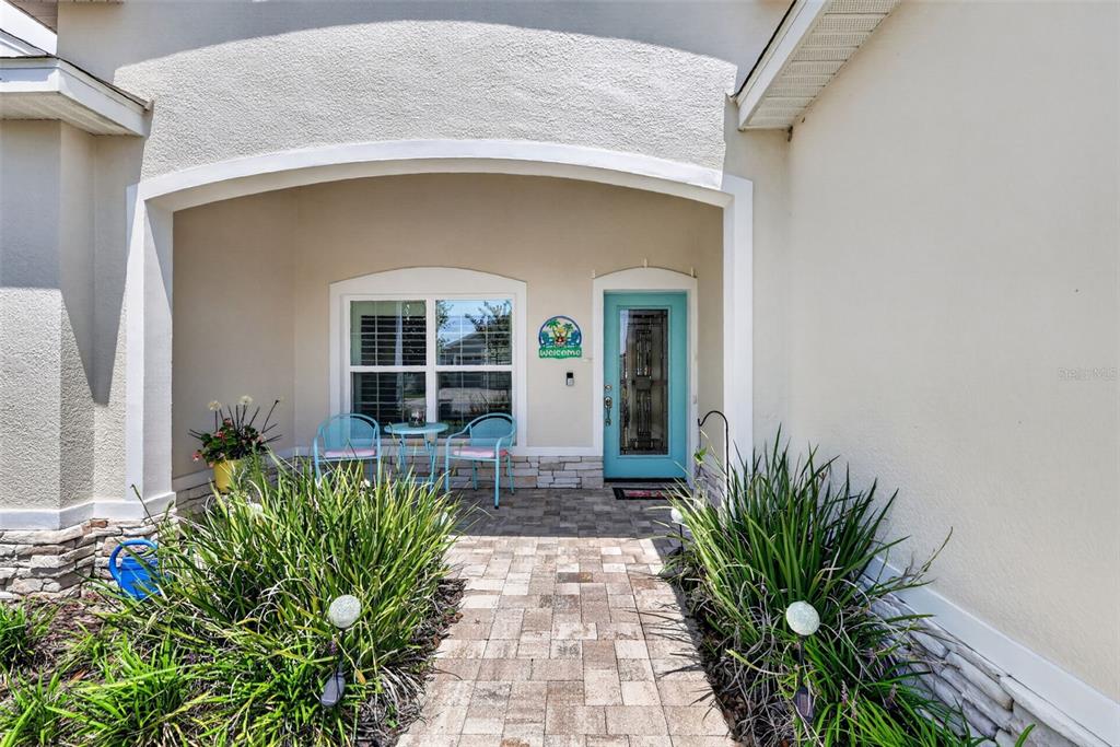 A paved walkway leads to a covered front porch with two chairs and a door — 12615 NE 49TH DRIVE, OXFORD, FL
