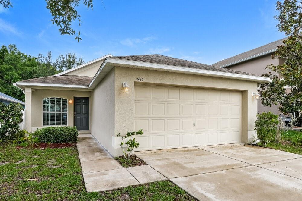 A single-story house with a beige stucco exterior, a two-car garage, and a front walkway — 3457 BELLERICAY LANE, LAND O LAKES, FL