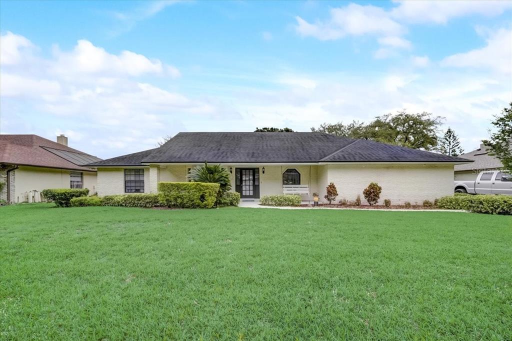 A single-story white brick house with a dark roof and a large front lawn — 7233 BRANCHTREE DRIVE, ORLANDO, FL