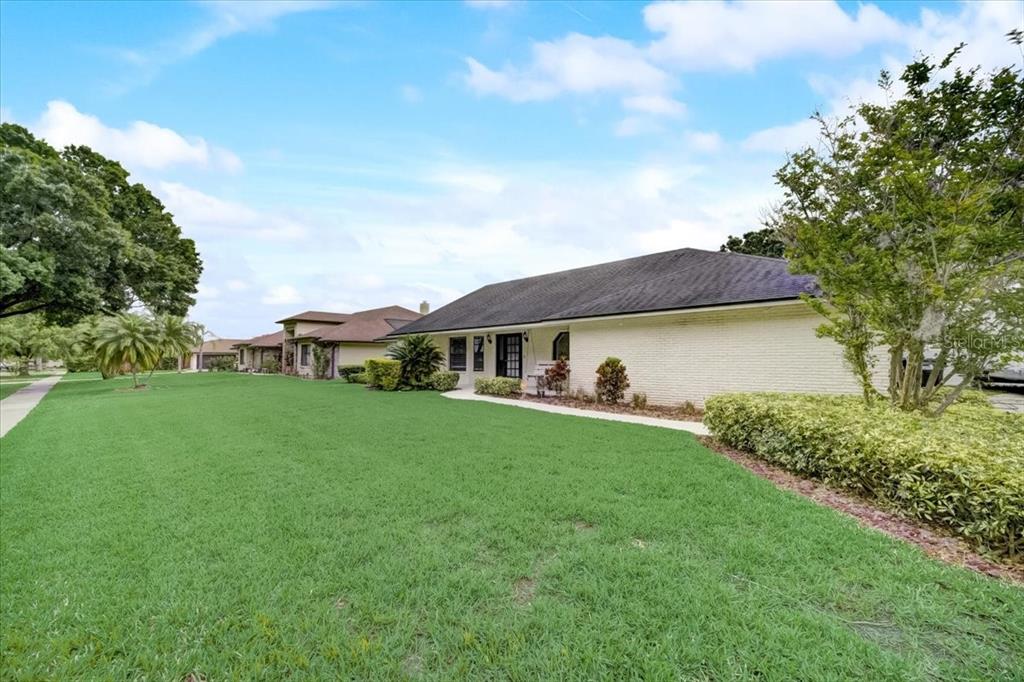 A side view of a single-story brick house with a large lawn and landscaping — 7233 BRANCHTREE DRIVE, ORLANDO, FL