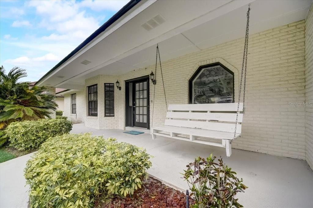 A white brick house exterior features a covered porch with a hanging wooden bench — 7233 BRANCHTREE DRIVE, ORLANDO, FL