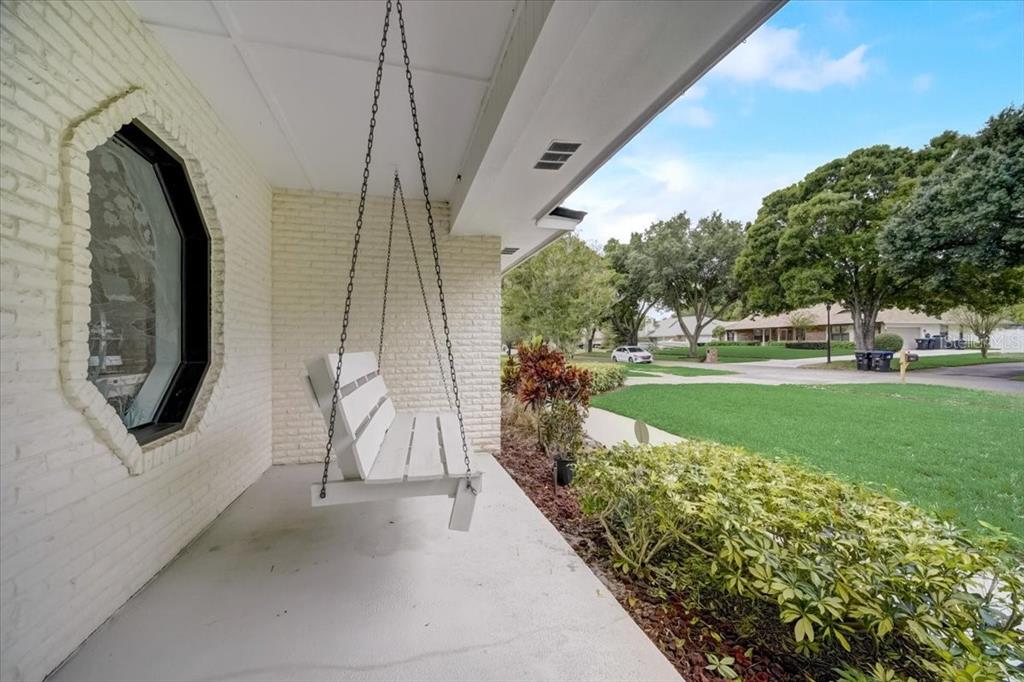A white porch swing hangs on a covered patio with a white brick wall — 7233 BRANCHTREE DRIVE, ORLANDO, FL