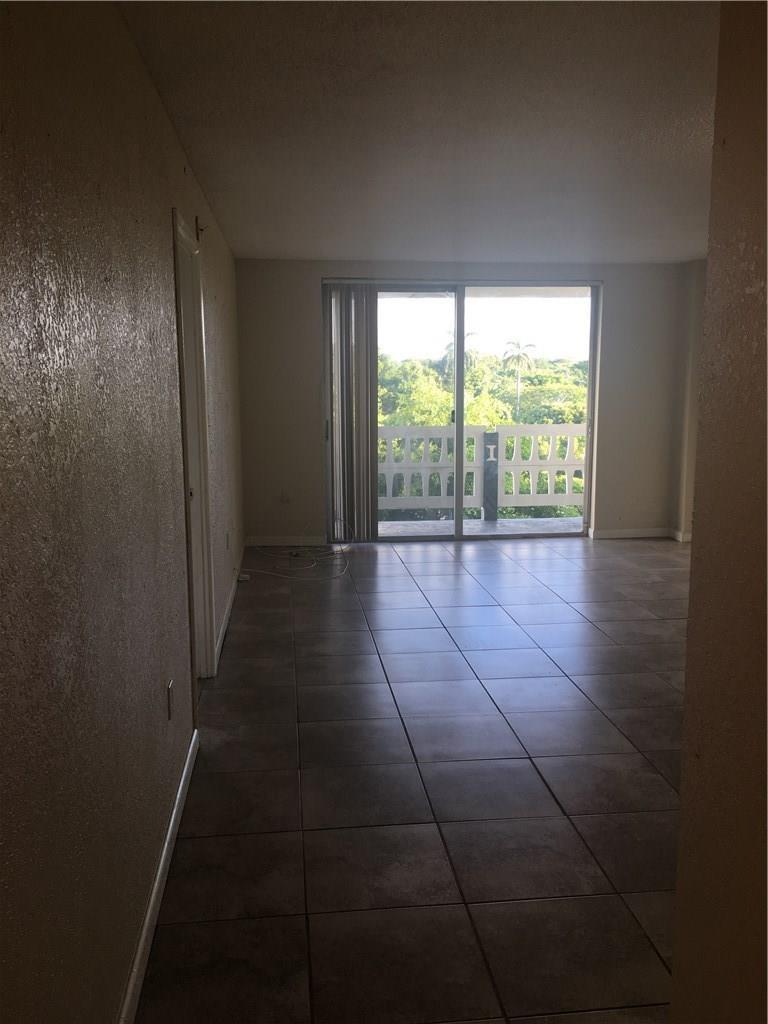 An empty living room with brown tile flooring and a sliding glass door to a balcony — 15600 NW 7th Avenue # 421, Miami FL 33169, MIAMI, FL