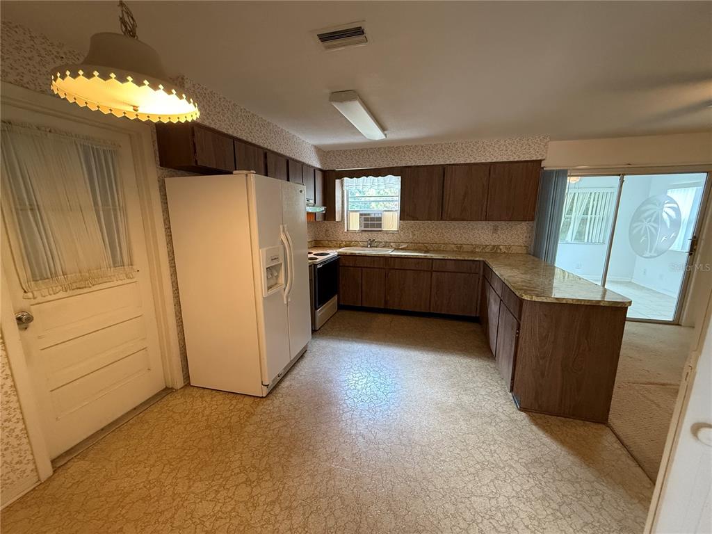 A kitchen features wood cabinets, a white refrigerator, a patterned floor, and a sliding door — 27 KATHY DRIVE, ORMOND BEACH, FL
