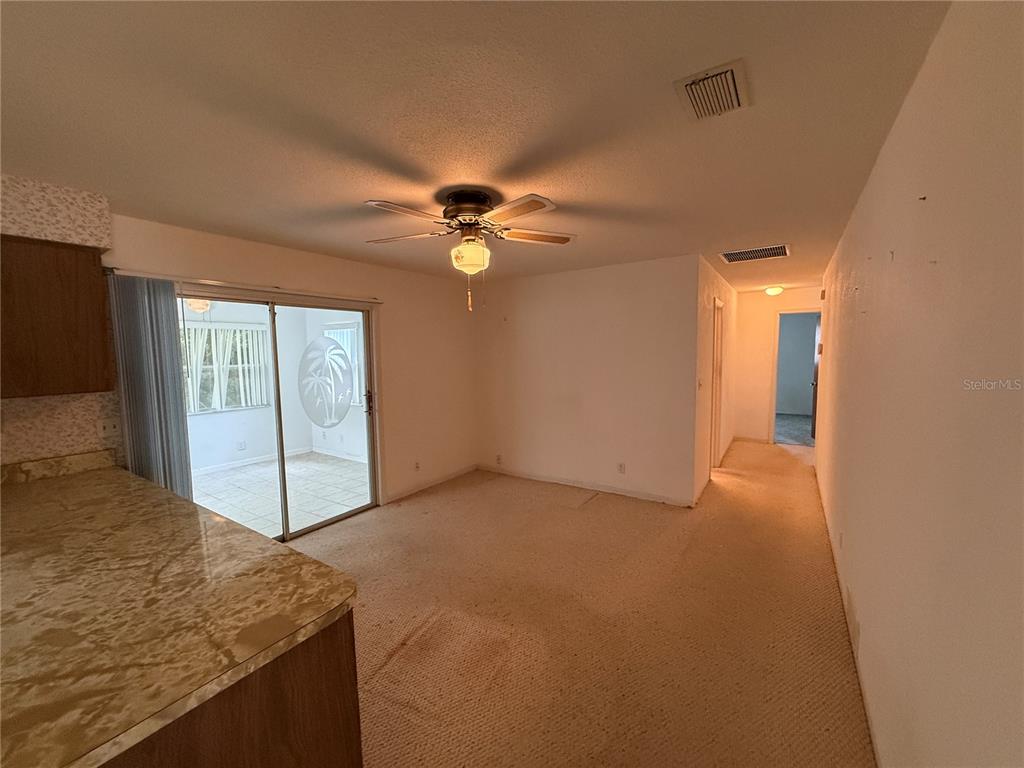 A carpeted living room features a ceiling fan, sliding glass doors, and an adjacent kitchen — 27 KATHY DRIVE, ORMOND BEACH, FL
