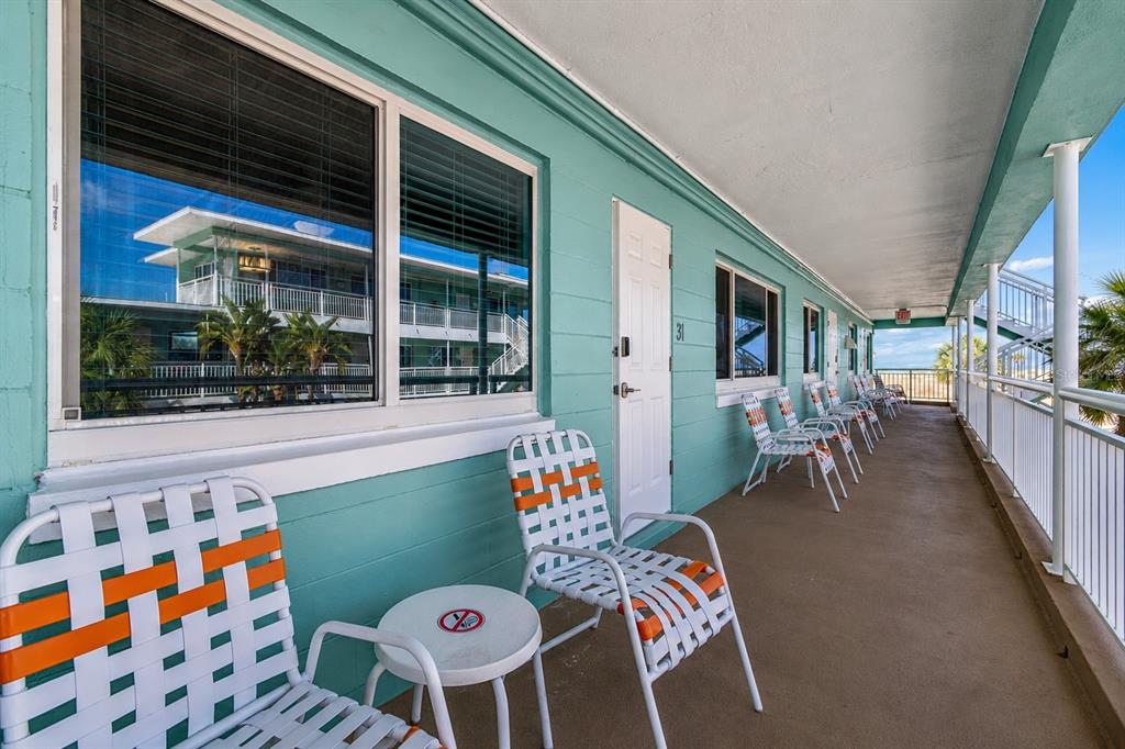 An outdoor balcony with teal walls features several orange and white woven chairs and tables — 11730 GULF BOULEVARD UNIT 31, TREASURE ISLAND, FL