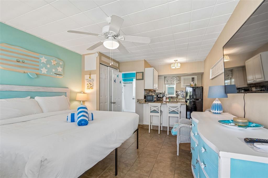 A studio apartment features a bed, a small kitchen with bar seating, and tiled floors — 11730 GULF BOULEVARD UNIT 31, TREASURE ISLAND, FL