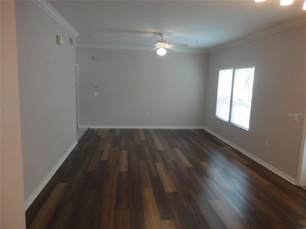An empty room features dark wood-look flooring, light gray walls, and a ceiling fan — 4820 SW 91ST TERRACE UNIT Q-202, GAINESVILLE, FL