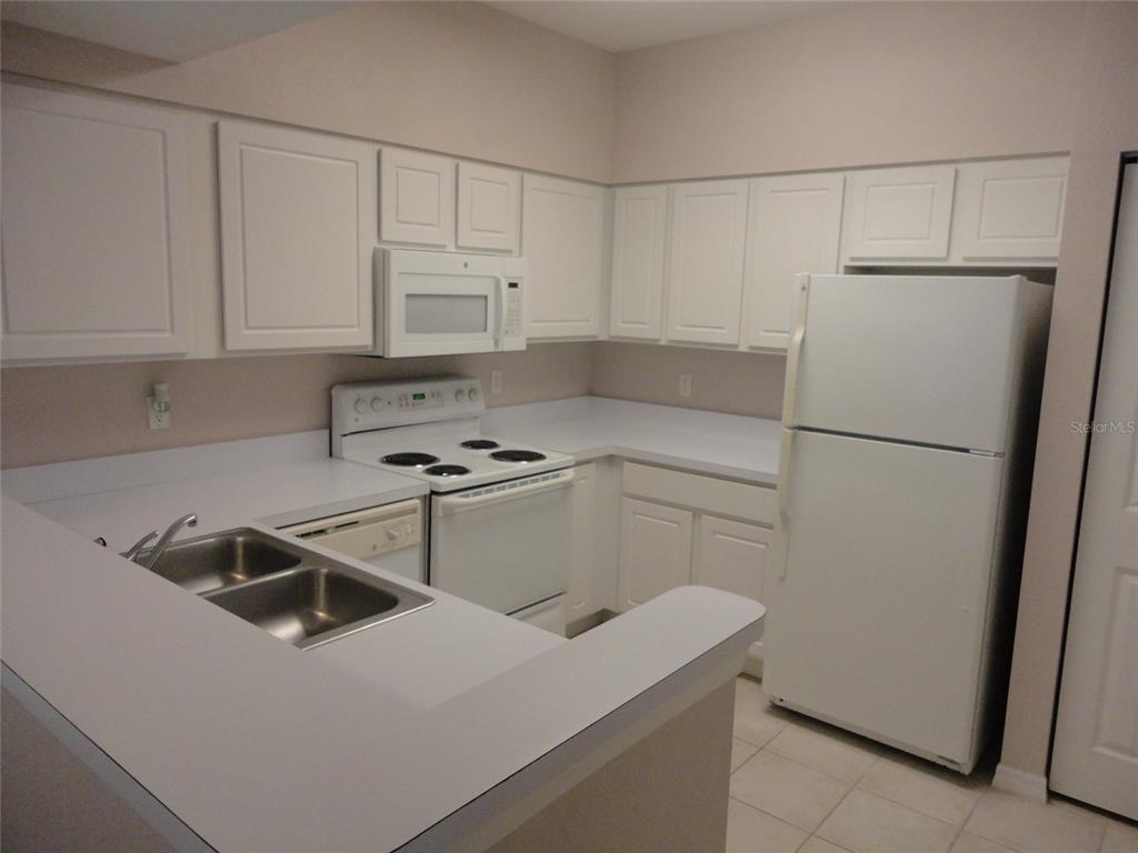 A kitchen features white cabinets, white appliances, a double sink, and light-colored countertops — 4820 SW 91ST TERRACE UNIT Q-202, GAINESVILLE, FL