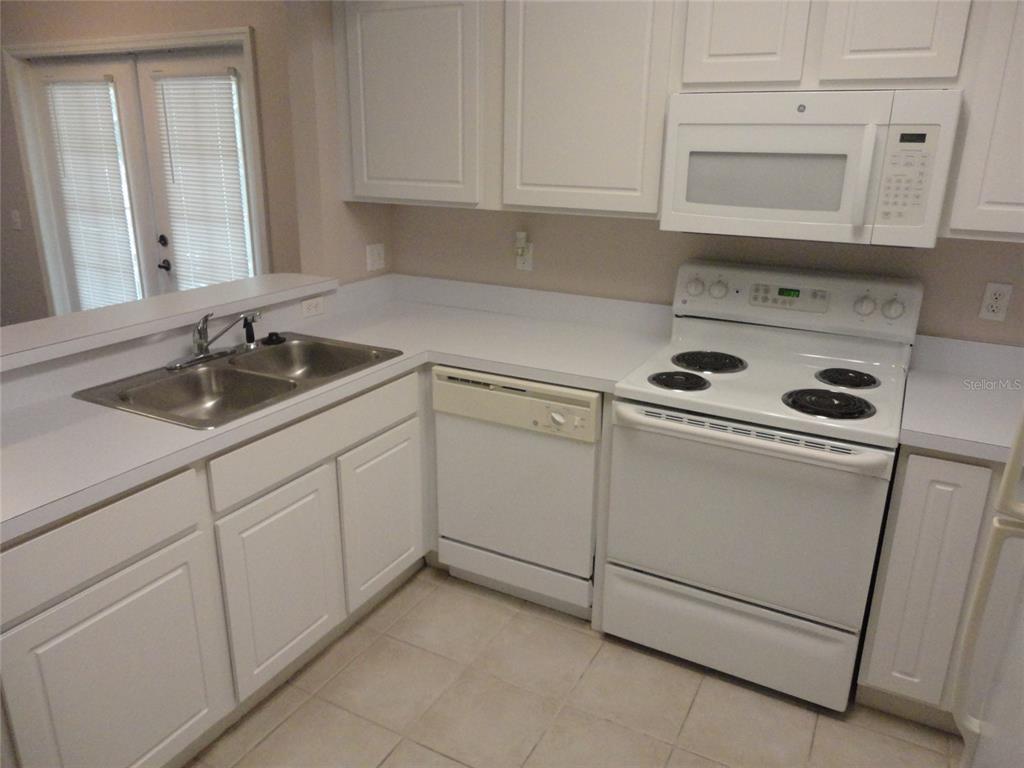 A kitchen features white cabinets, white appliances, a double sink, and light-colored tile flooring — 4820 SW 91ST TERRACE UNIT Q-202, GAINESVILLE, FL