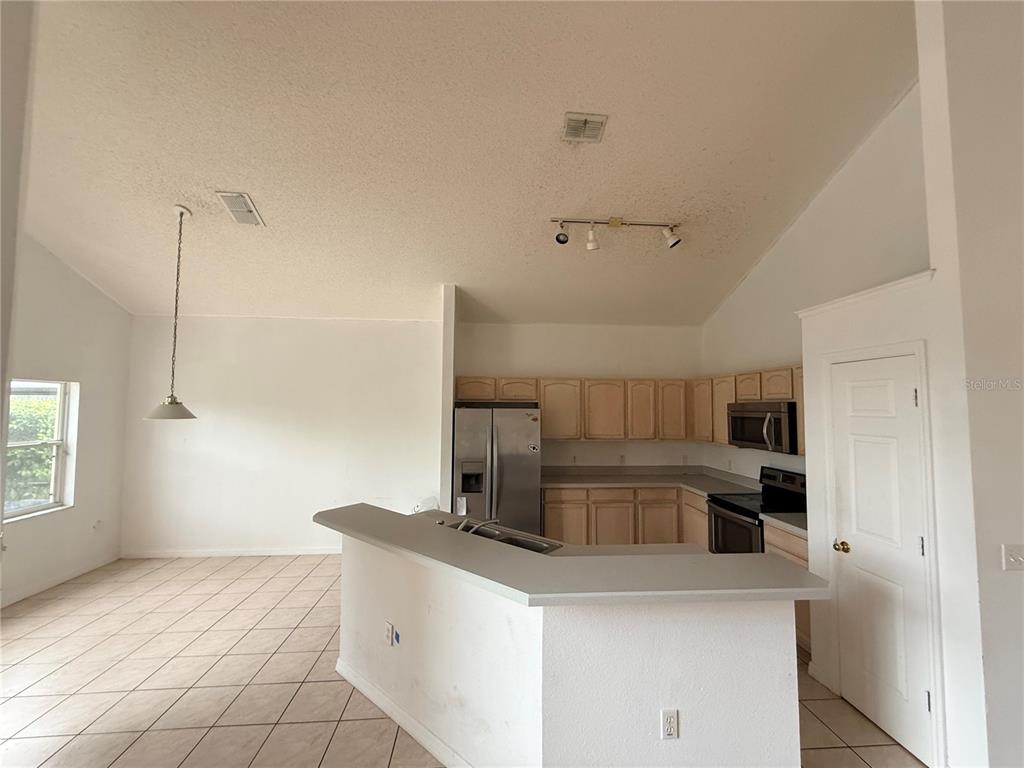 A kitchen with light wood cabinets, stainless steel appliances, and a breakfast bar — 2918 BLOOMING ALAMANDA LOOP, KISSIMMEE, FL