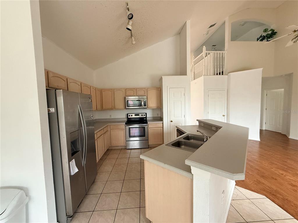 A kitchen with light wood cabinets, stainless steel appliances, and a breakfast bar island — 2918 BLOOMING ALAMANDA LOOP, KISSIMMEE, FL