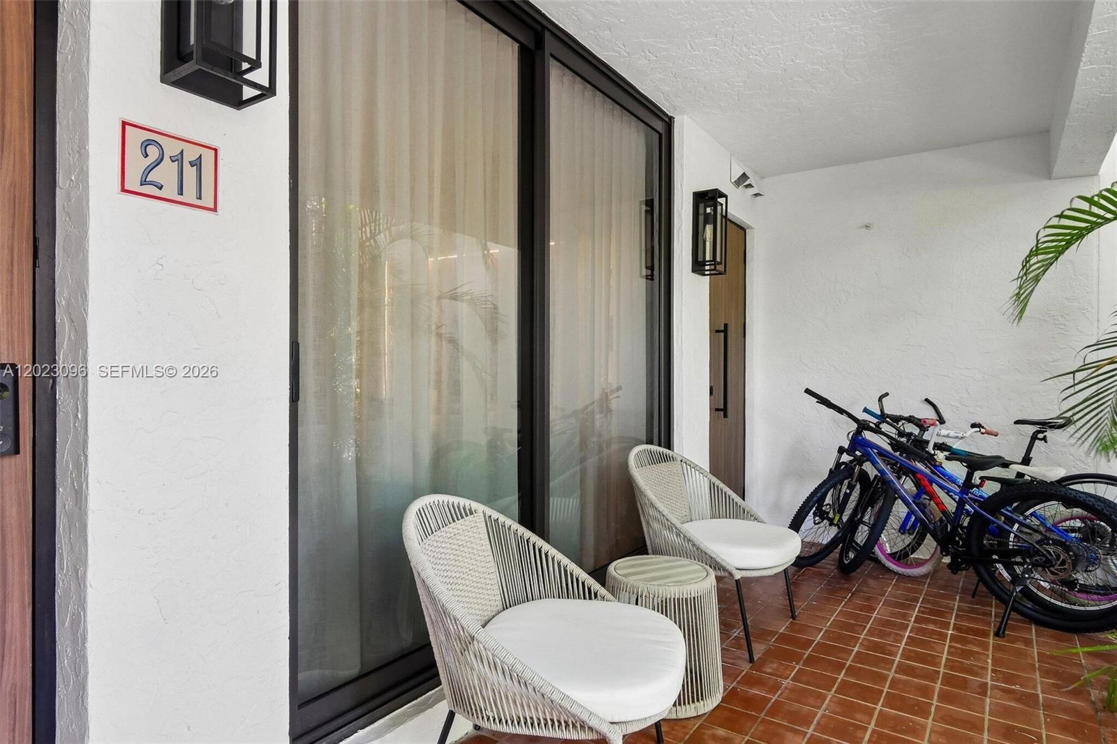A patio features two woven chairs, a small table, and several bicycles on tiled flooring — 425 Grapetree Dr # 211, Key Biscayne FL 33149, KEY BISCAYNE, FL