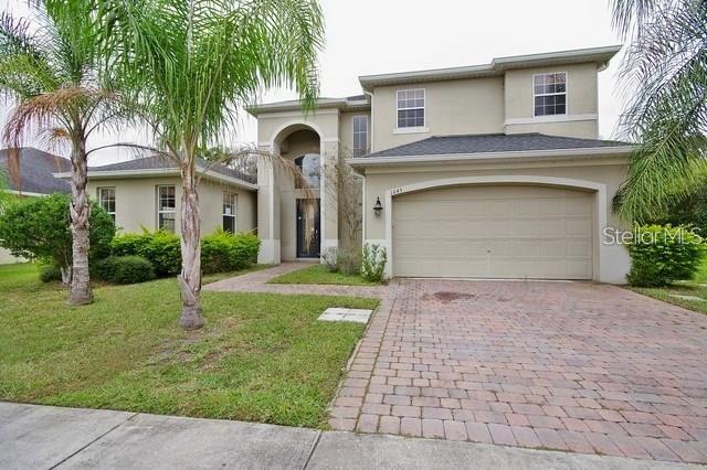 A two-story house with a tan stucco exterior, a brick driveway, and palm trees — 1643 STARGAZER TERRACE, SANFORD, FL