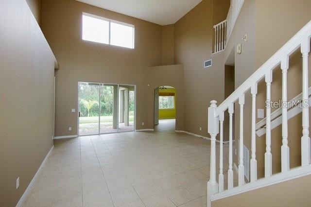 An open living area features high ceilings, tile flooring, and a white wooden staircase — 1643 STARGAZER TERRACE, SANFORD, FL