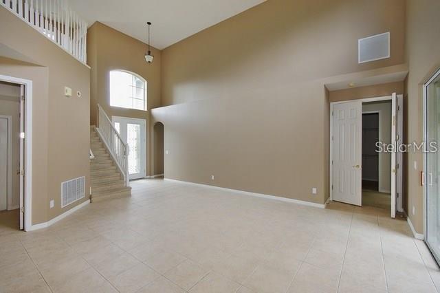 An empty living room with high ceilings, beige walls, tile flooring, and a staircase — 1643 STARGAZER TERRACE, SANFORD, FL