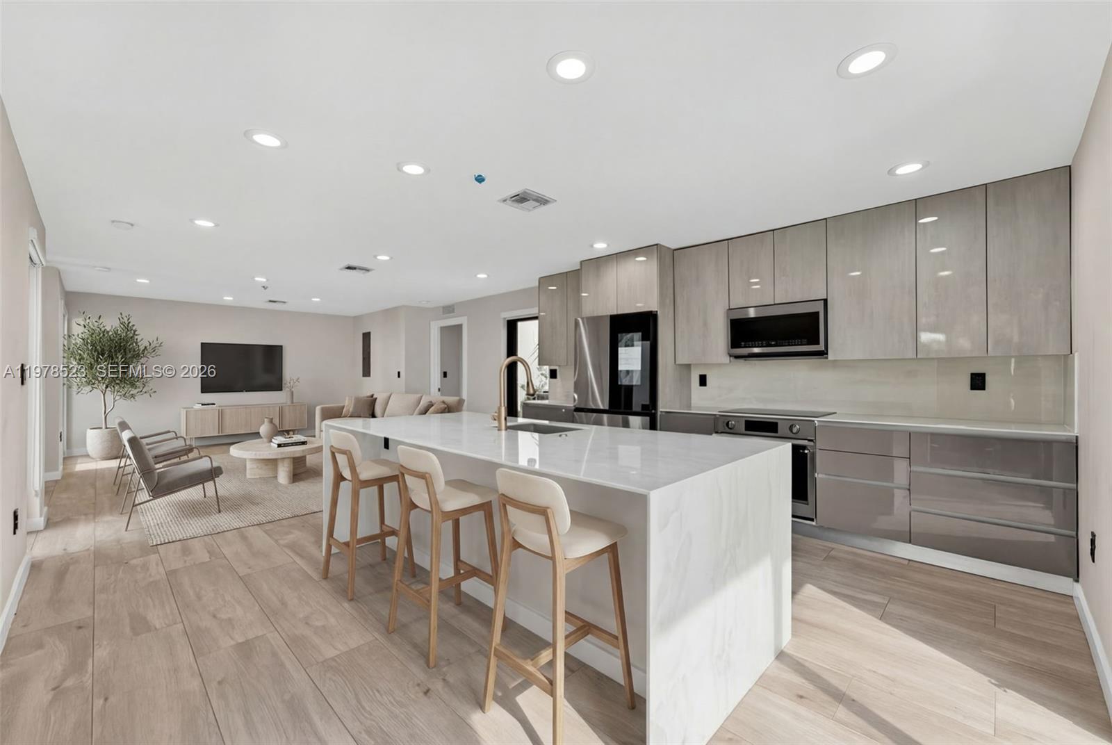 A modern open-concept kitchen features a marble-topped island, light wood cabinetry, and adjacent living area — 5101 N Miami Ave, Miami FL 33137, MIAMI, FL