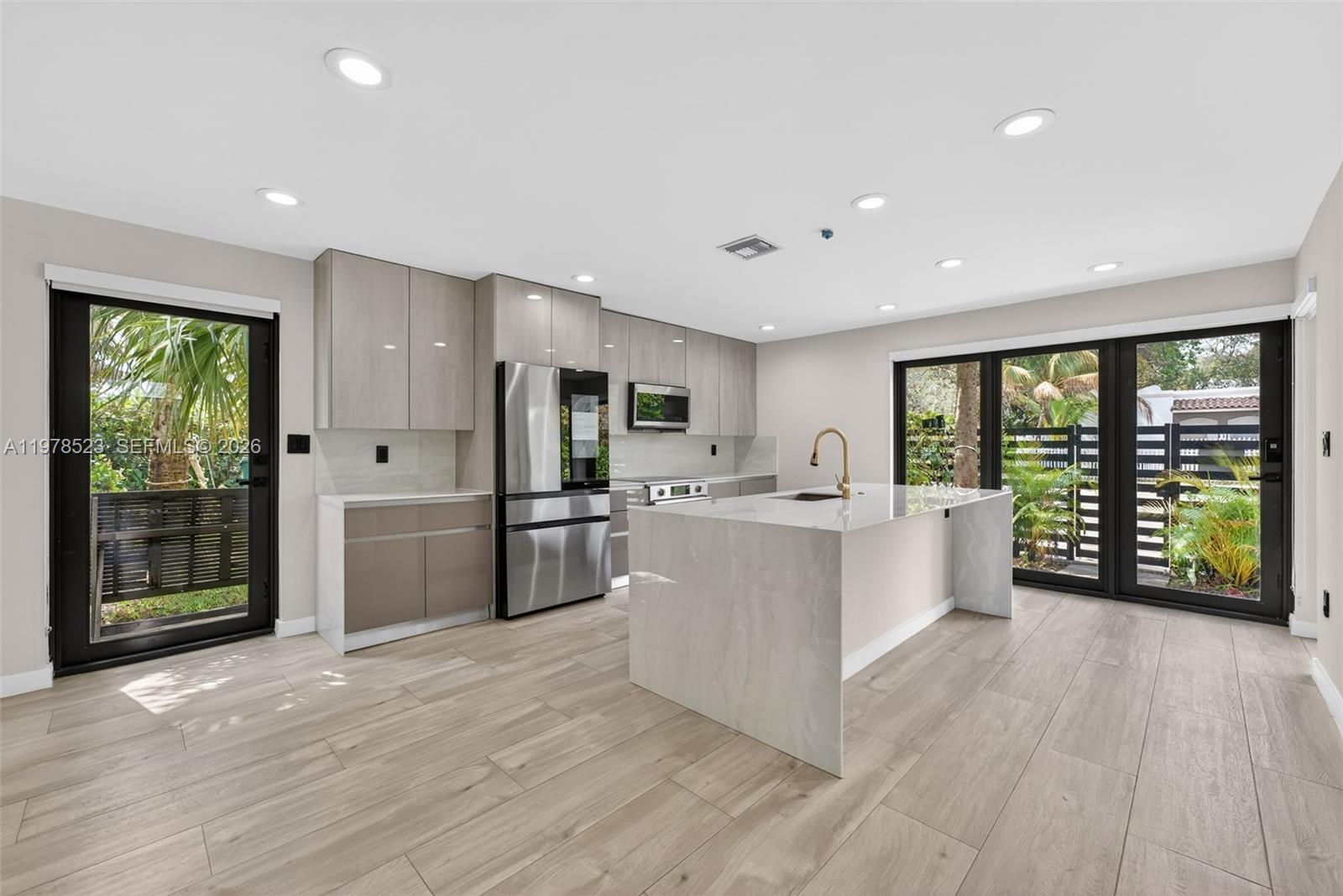 A modern kitchen features light wood cabinetry, a marble-topped island, and glass doors to outdoors — 5101 N Miami Ave, Miami FL 33137, MIAMI, FL