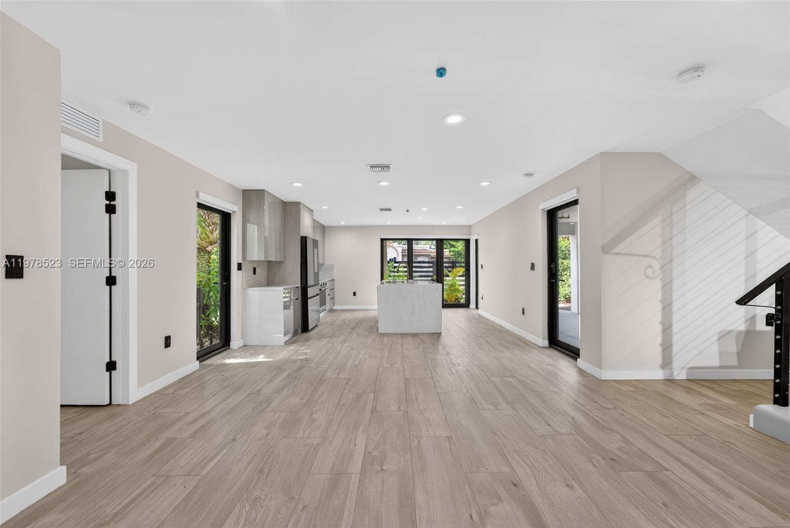 This open-concept kitchen and living area features light wood-look tile flooring and white cabinetry — 5101 N Miami Ave, Miami FL 33137, MIAMI, FL