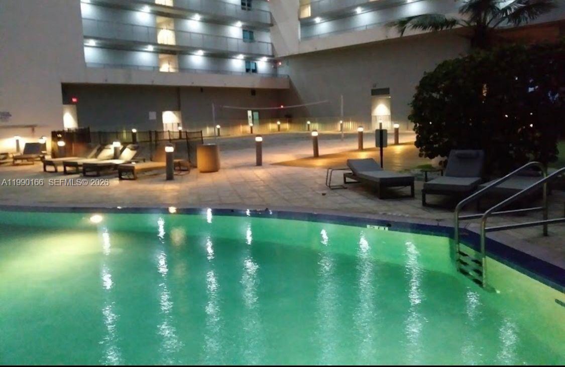 A swimming pool sits in the foreground of a multi-story building with lounge chairs nearby — 888 Biscayne Blvd # 1810, Miami FL 33132, MIAMI, FL