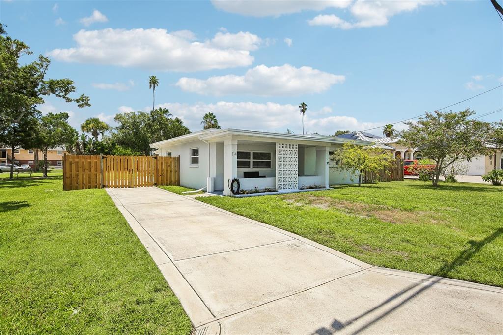 A single-story white house features a concrete driveway, a wooden fence, and a covered porch — 114 LAKE JUDY LEE DRIVE, LARGO, FL