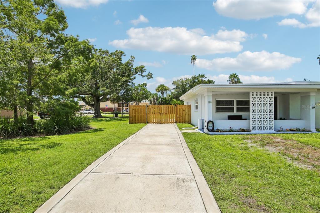 A concrete driveway leads to a white house with a wooden gate and decorative block wall — 114 LAKE JUDY LEE DRIVE, LARGO, FL
