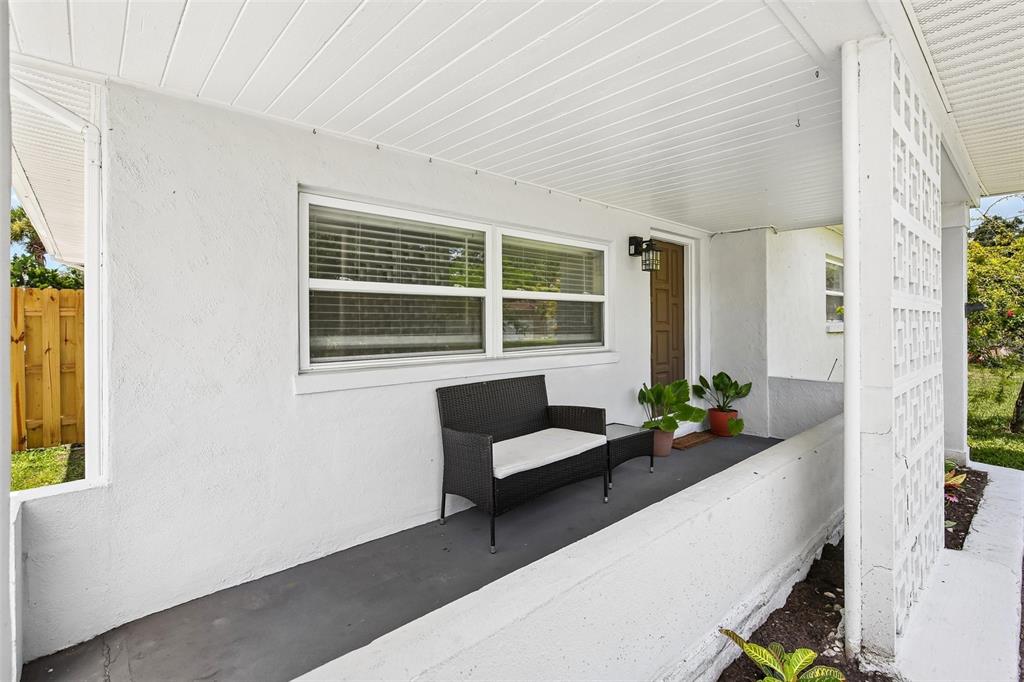 A covered front porch features a white stucco exterior, a black bench, and decorative block columns — 114 LAKE JUDY LEE DRIVE, LARGO, FL