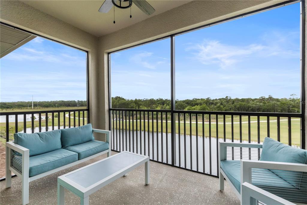 A screened-in patio features outdoor furniture overlooking a pond and a wooded golf course — 18008 GAWTHROP DRIVE UNIT 402, LAKEWOOD RANCH, FL