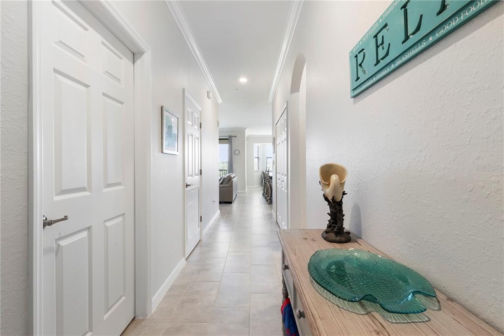 A hallway with light tile flooring leads toward a living area with white walls — 18008 GAWTHROP DRIVE UNIT 402, LAKEWOOD RANCH, FL