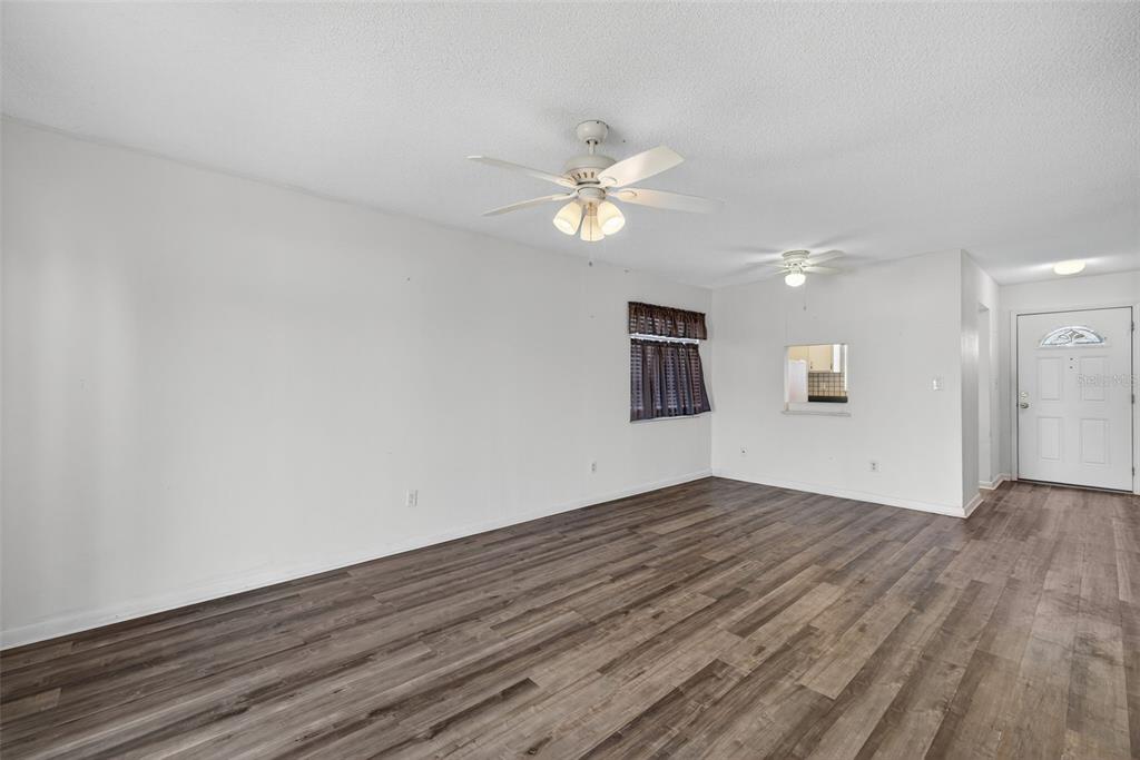 An empty living room features wood-look flooring, white walls, and two ceiling fans — 2207 CROTON COURT UNIT 0, LEHIGH ACRES, FL