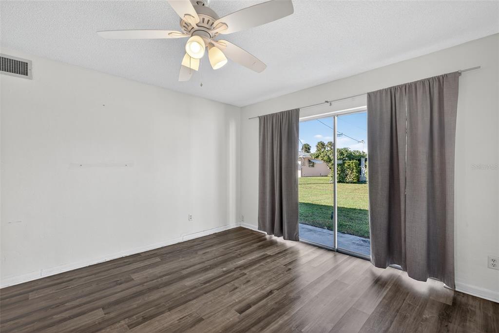 An empty room features wood-look flooring, a ceiling fan, and sliding glass doors with curtains — 2207 CROTON COURT UNIT 0, LEHIGH ACRES, FL