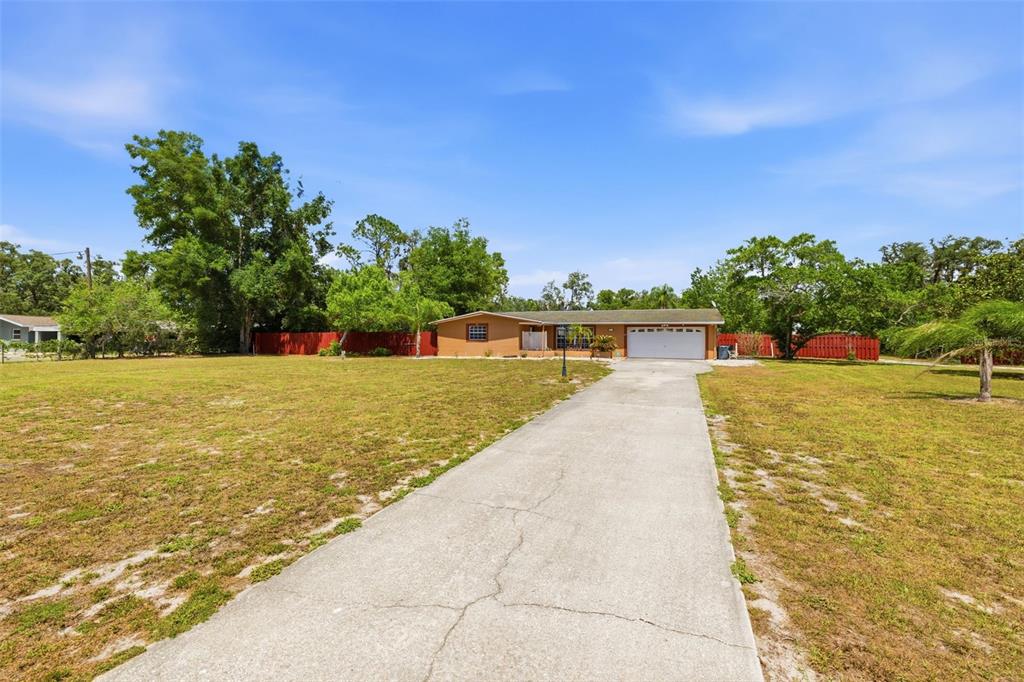 A single-story house with a white garage door sits at the end of a long driveway — 10744 OSCEOLA DRIVE, NEW PORT RICHEY, FL