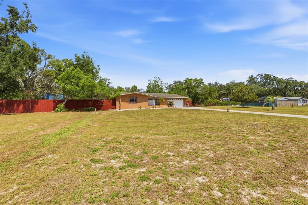 A single-story house with a garage sits on a large, grassy lot with trees — 10744 OSCEOLA DRIVE, NEW PORT RICHEY, FL