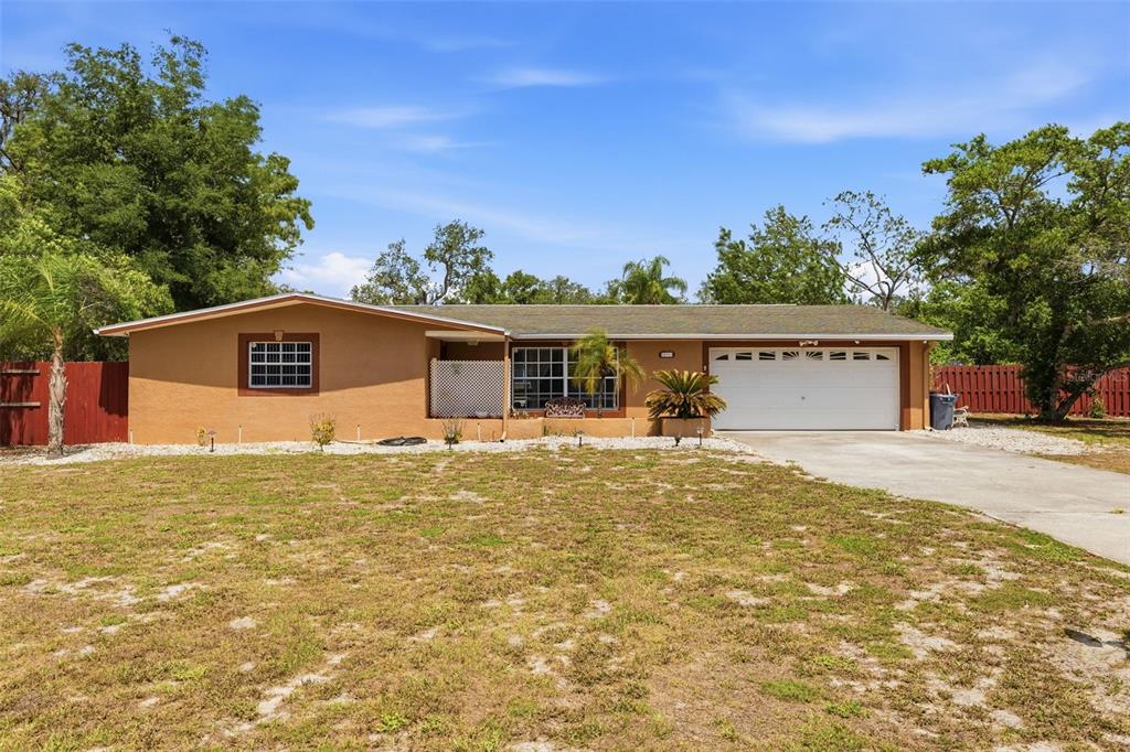 A single-story house with a tan stucco exterior, a two-car garage, and a large yard — 10744 OSCEOLA DRIVE, NEW PORT RICHEY, FL