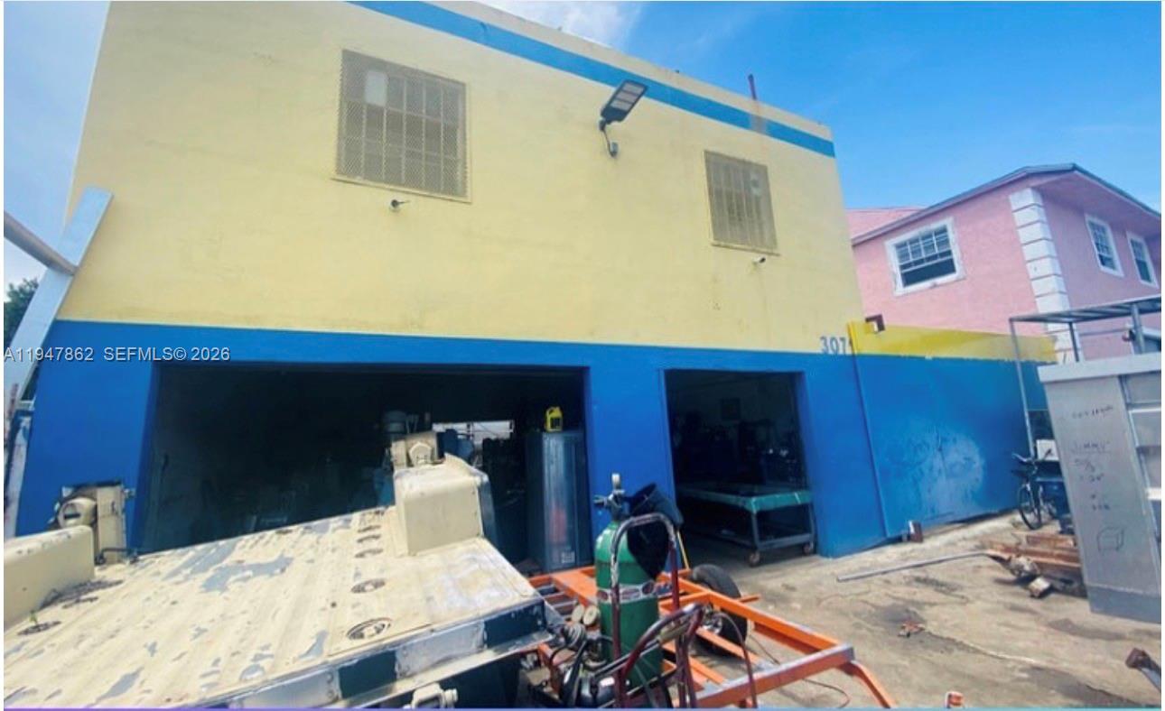 A two-story yellow and blue commercial building with open garage bays and outdoor equipment — 3071 NW 54th St, Miami FL 33142, MIAMI, FL