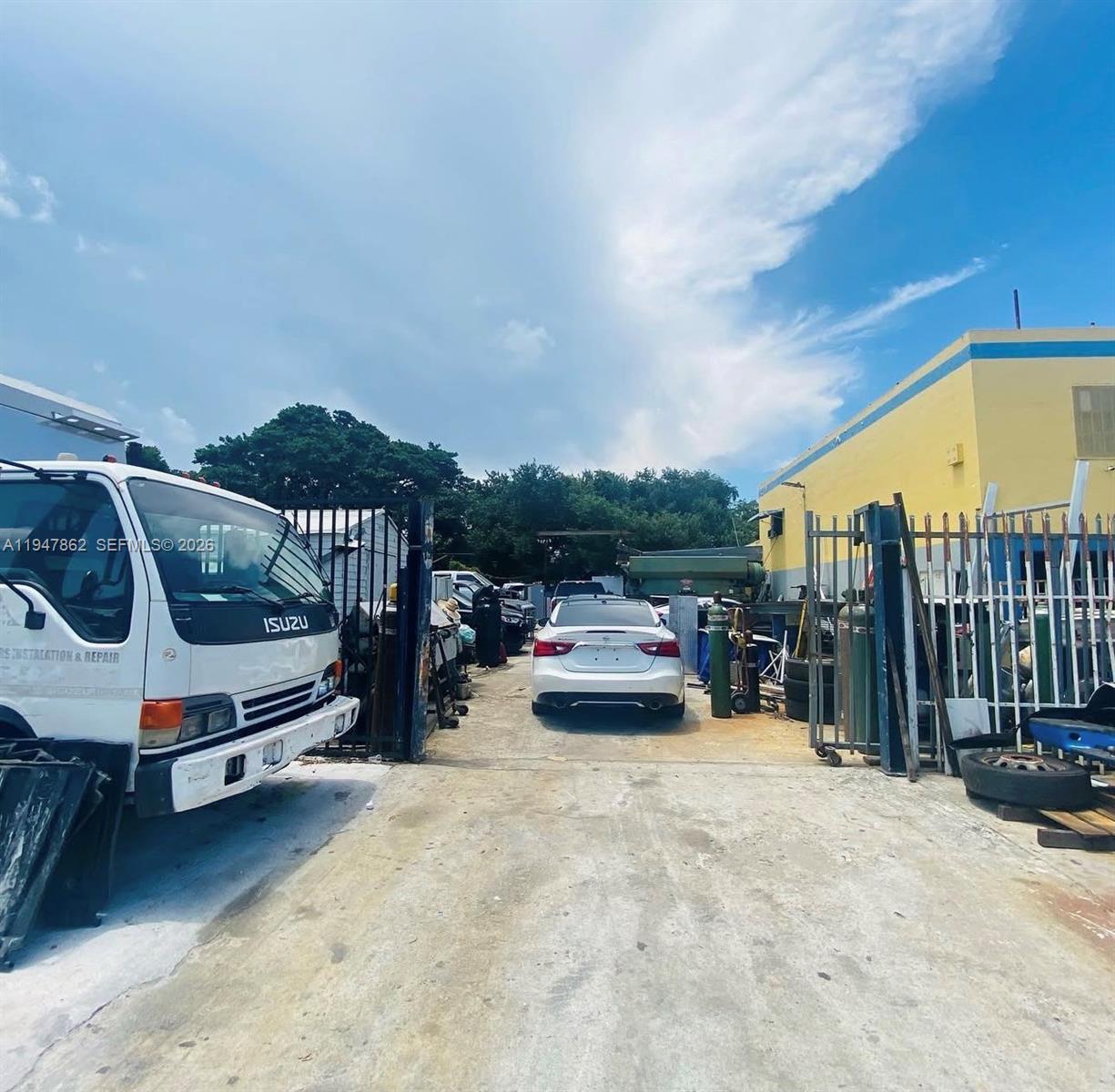 An outdoor industrial lot features a white Isuzu truck, a white sedan, and yellow buildings — 3071 NW 54th St, Miami FL 33142, MIAMI, FL