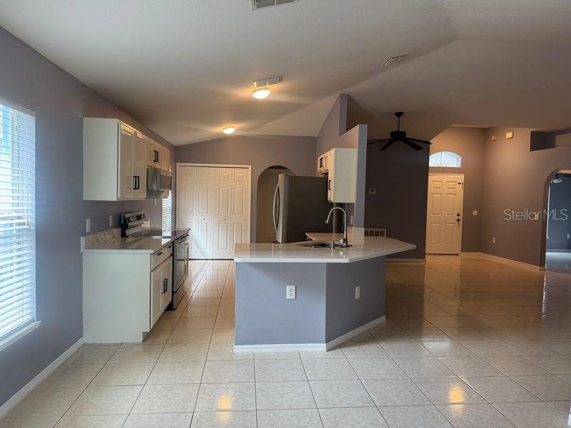A kitchen with white cabinets, light countertops, and tile flooring opens to a living area — 3226 BELLERICAY LANE, LAND O LAKES, FL