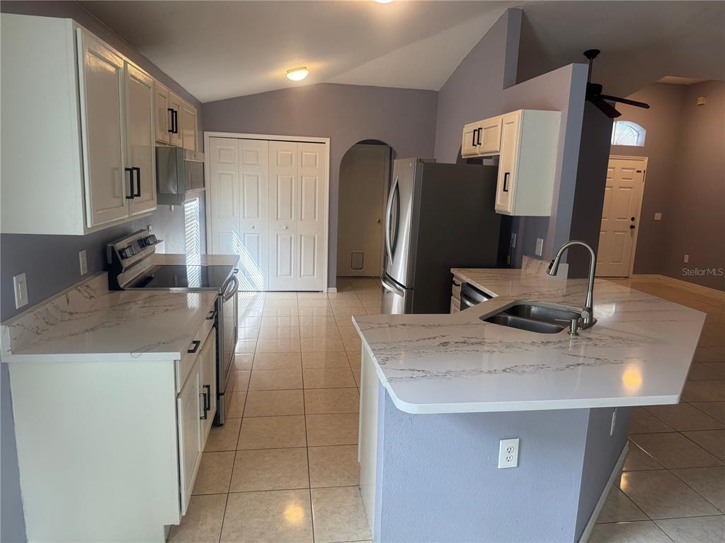 A kitchen features white cabinets, quartz countertops, stainless steel appliances, and light-colored tile flooring — 3226 BELLERICAY LANE, LAND O LAKES, FL