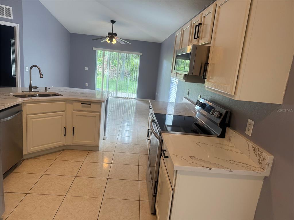 A kitchen with white cabinets, marble-look countertops, stainless steel appliances, and tile flooring — 3226 BELLERICAY LANE, LAND O LAKES, FL