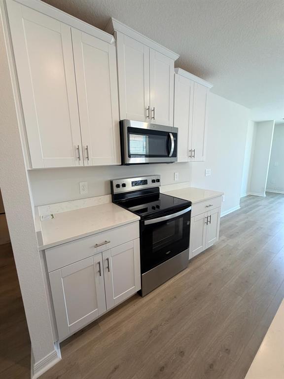 A kitchen features white cabinets, stainless steel appliances, and light-colored countertops over wood-look flooring — 5229 NATIVE MILE LOOP, DAVENPORT, FL