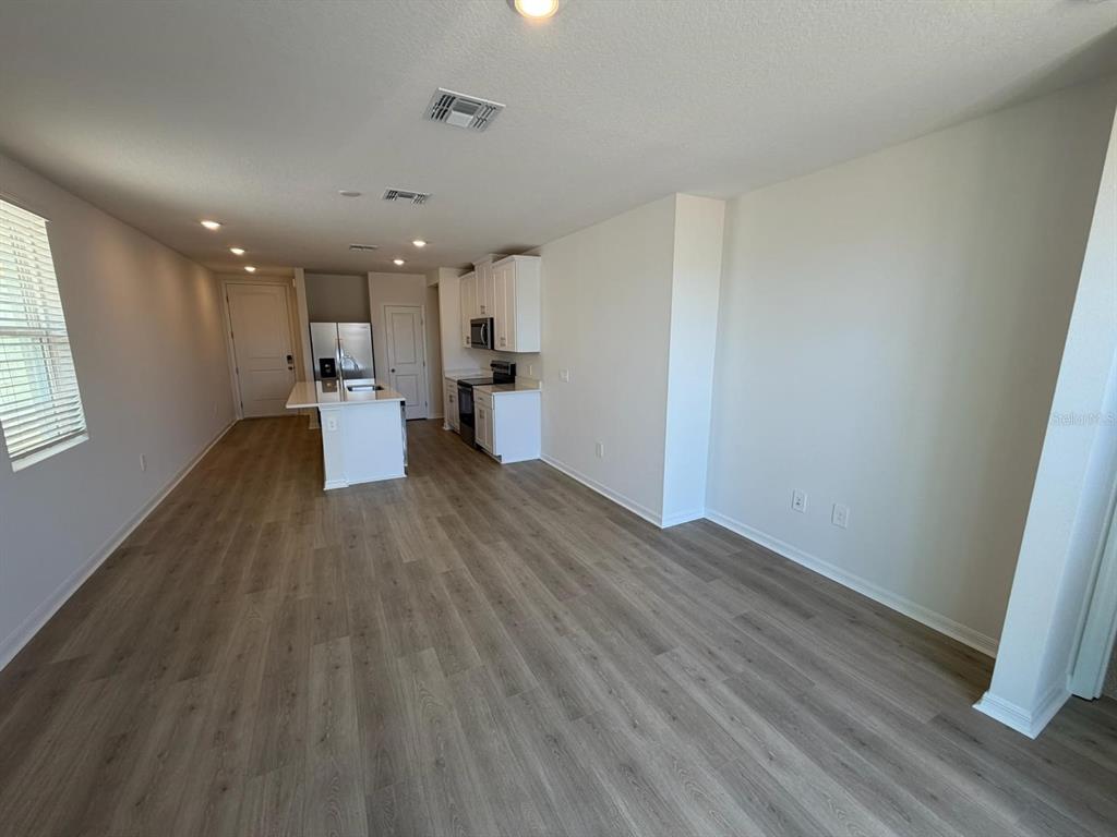 An open-concept kitchen and living area features white cabinetry, a center island, and wood-look flooring — 5229 NATIVE MILE LOOP, DAVENPORT, FL