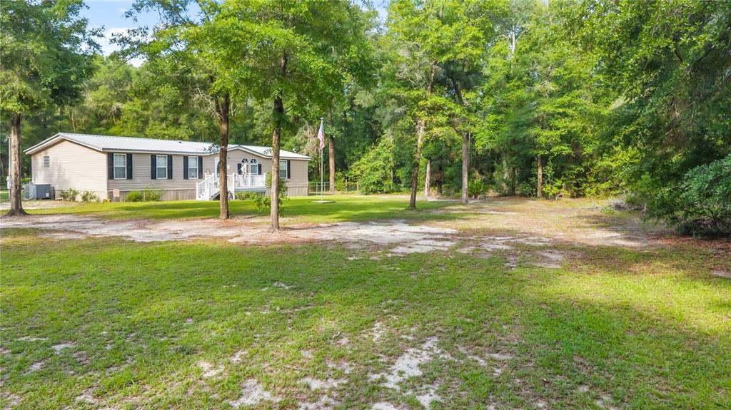 A single-story manufactured home sits on a grassy lot surrounded by mature trees — 6679 NW 27TH PLACE, BELL, FL