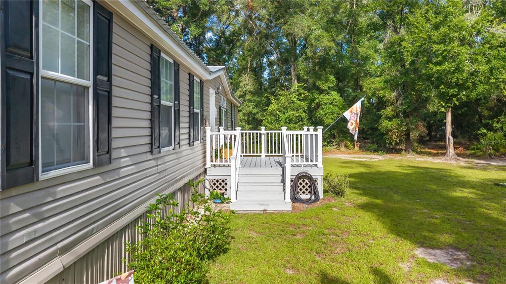 A light gray mobile home features a small wooden deck with white railings and stairs — 6679 NW 27TH PLACE, BELL, FL