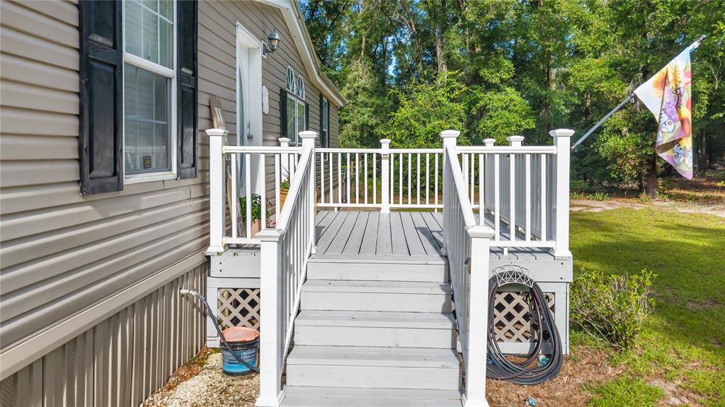 A gray wooden deck with white railings and stairs sits beside a tan mobile home — 6679 NW 27TH PLACE, BELL, FL