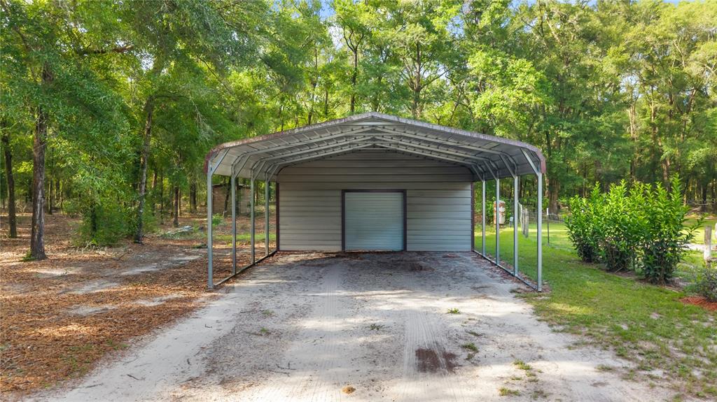 A metal carport with an enclosed storage unit stands on a sandy lot among trees — 6679 NW 27TH PLACE, BELL, FL