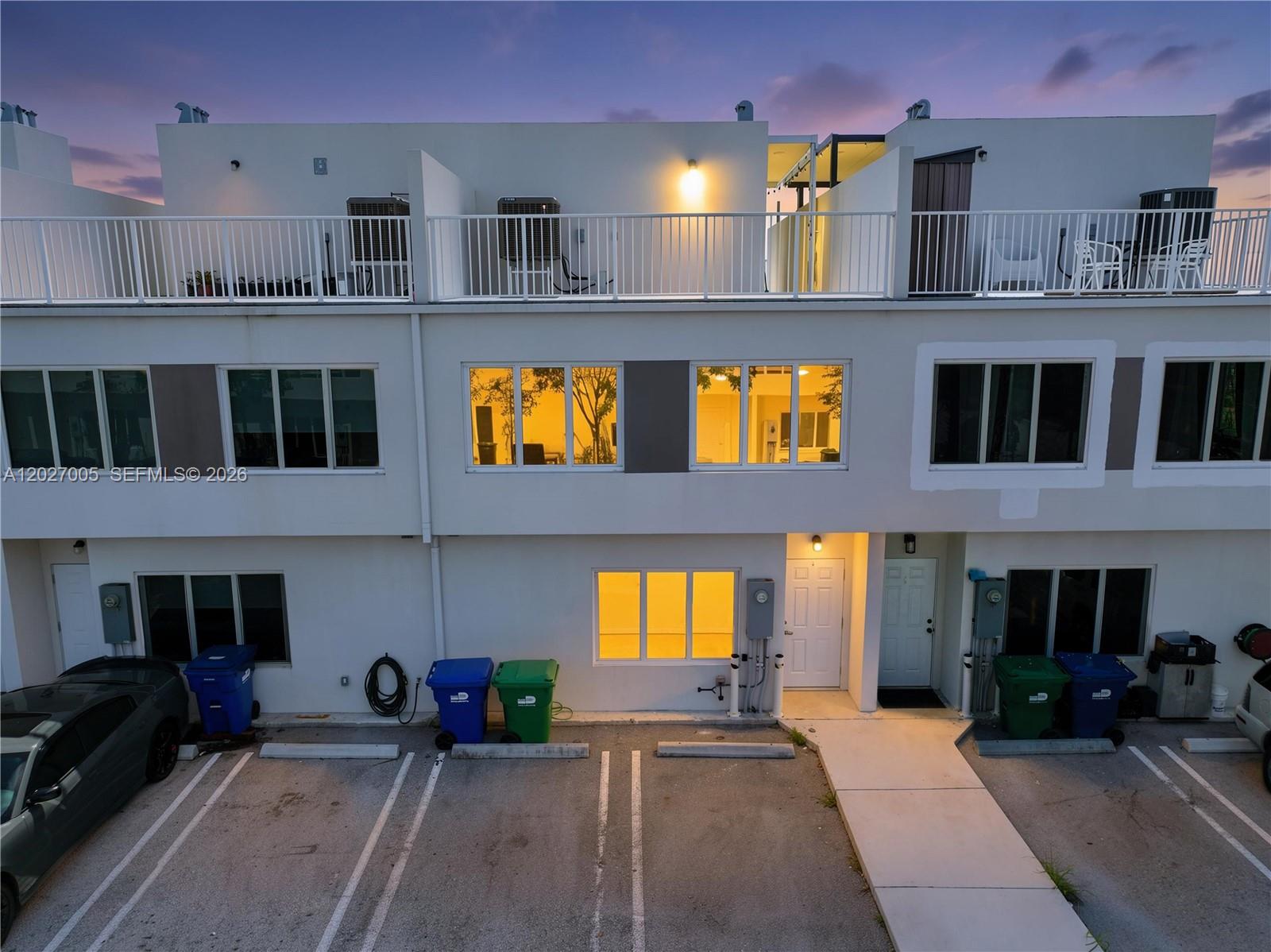 An exterior view of a multi-story townhouse complex with parking spaces and trash bins — 25813 SW 145th Ave, Homestead FL 33032, HOMESTEAD, FL