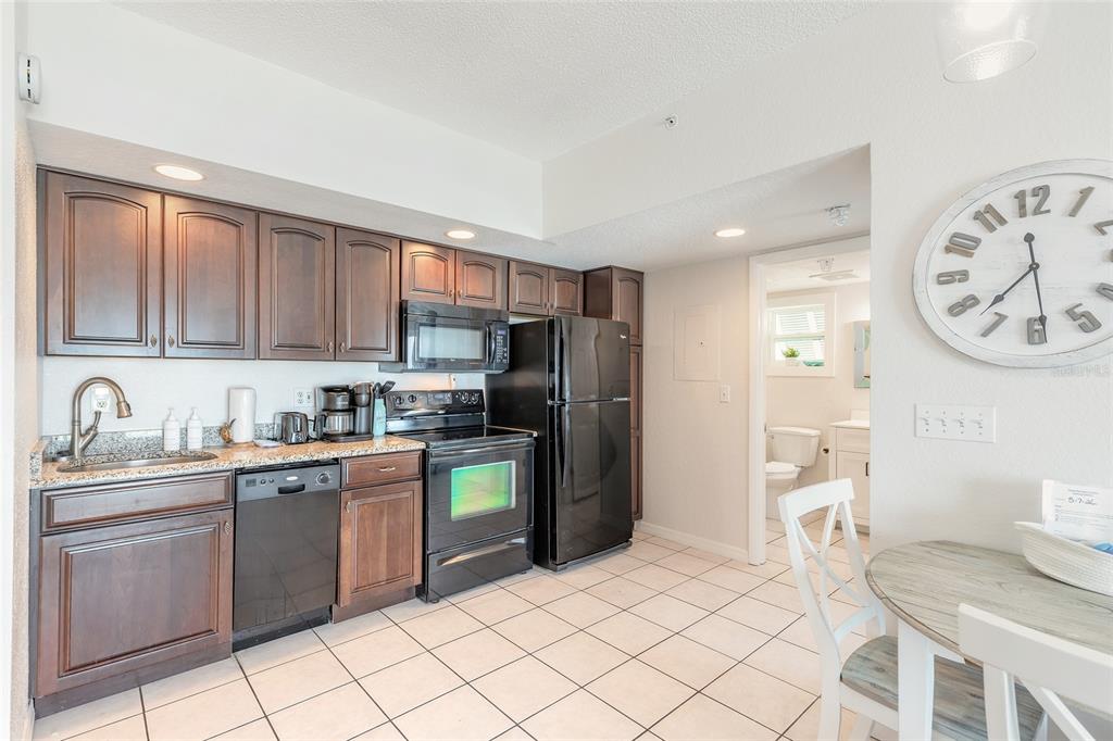 A kitchen features dark wood cabinets, black appliances, granite countertops, and white tile flooring — 611 S ATLANTIC AVENUE UNIT 4312, NEW SMYRNA BEACH, FL